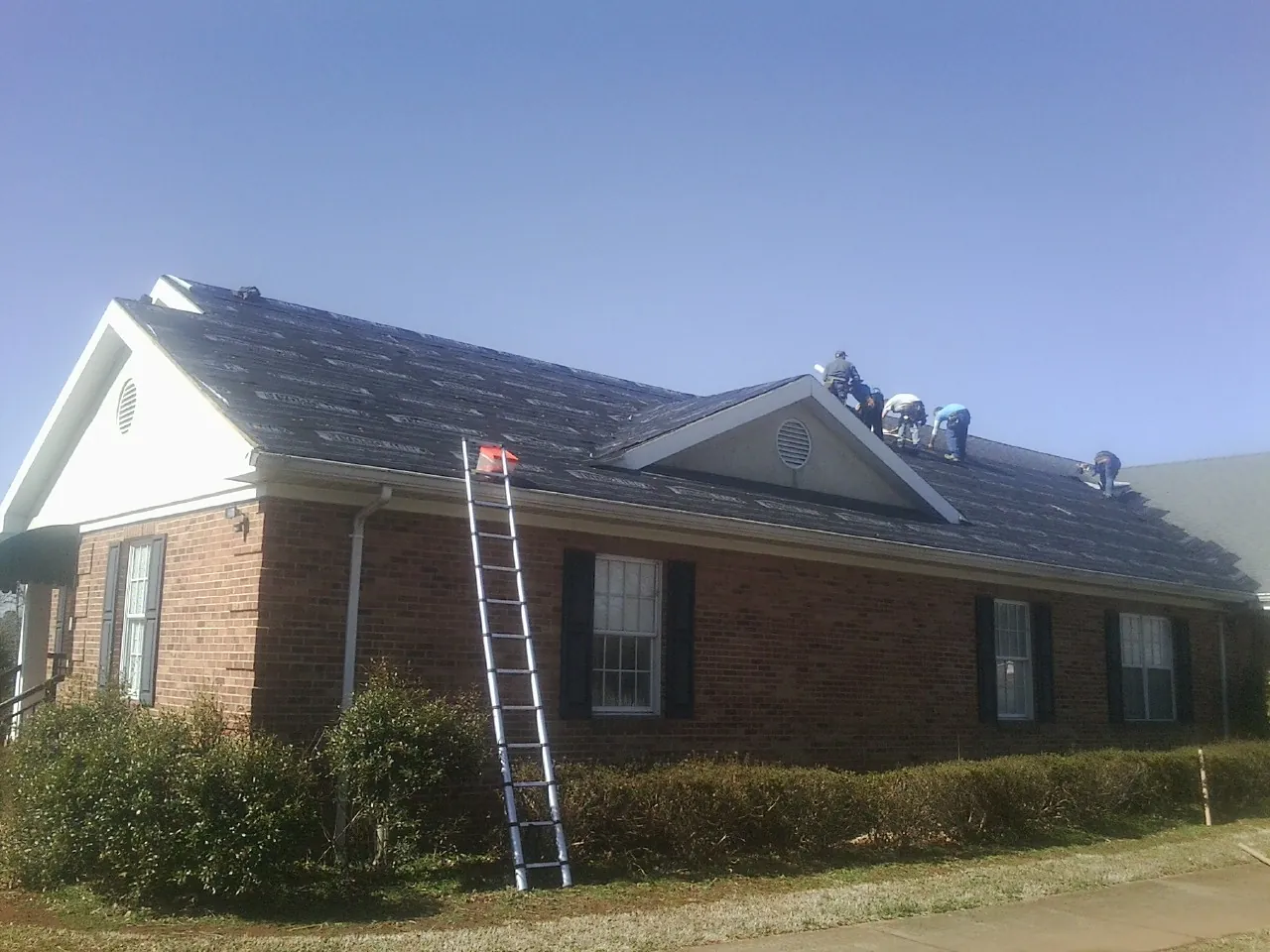 Crew tearing shingles off a brick ranch roof with a ladder set — Metal Roof Repair work by our crew in Rineyville