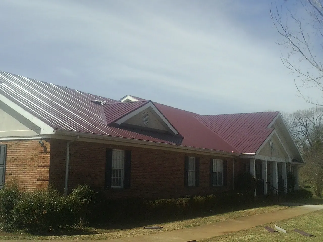 Red metal roof with gabled entries on a long brick building, from a Hail Damage Roof Repair job in Rineyville