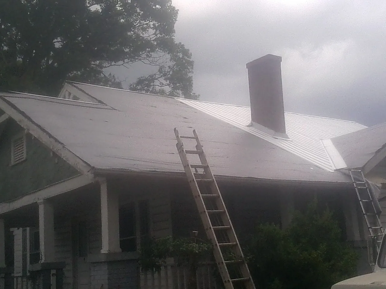 Ladders against a metal roof on an older home with a brick chimney in Rineyville