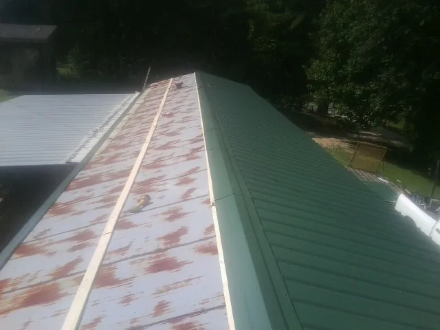 Old rusted panels beside newly installed green metal roofing — Wind Damage Roof Repair by Roofing Brothers in Rineyville