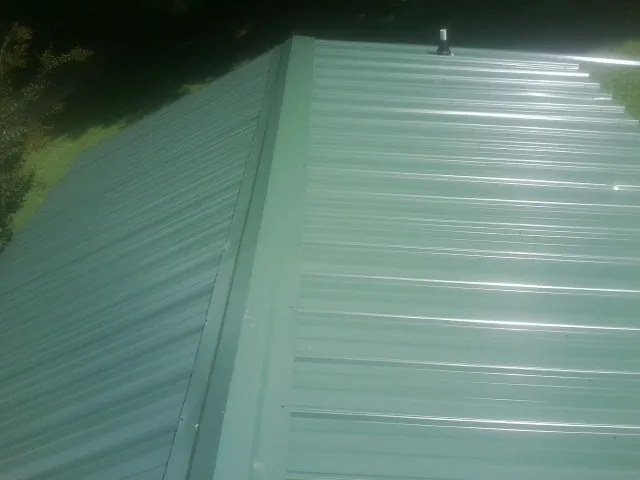 New green metal panels meeting at the ridge of a roof — Flat Roof Repair work by our crew in Rineyville
