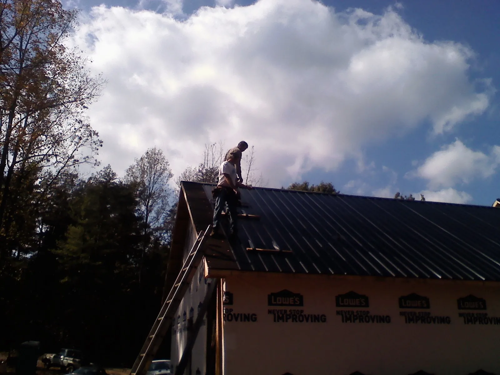 Roofer fastening dark metal panels high against a cloudy sky, from a Roof Inspection job in Rineyville