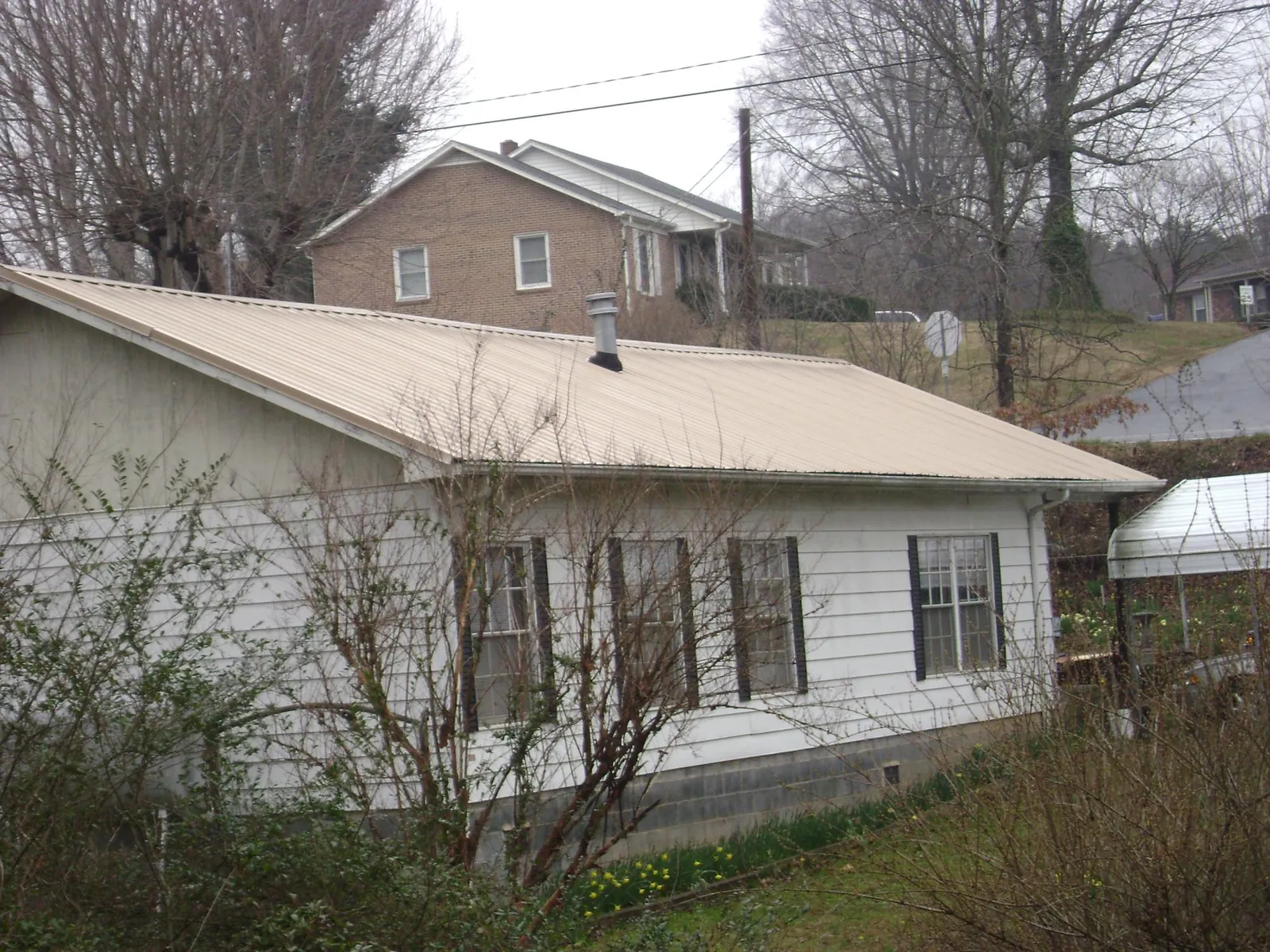 Tan metal roof on a white sided house set into a hillside — Commercial Roofing by Roofing Brothers in Rineyville